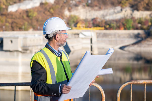 istock A bearded and bespectacled engineer with a blueprint in his hands in front of a dam retaining wall. 1473520147