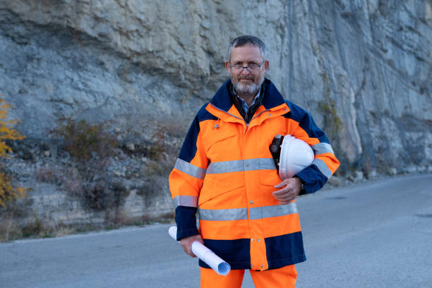 istock Engineer in white helmet, orange-blue safety reflective suit, and blueprints. 1473520204