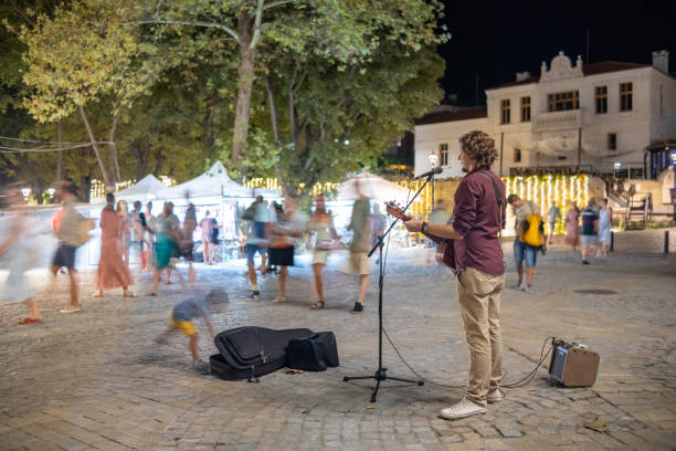 ein straßenmusiker spielt und singt für passanten auf einem platz eines kleinen ferienortes. - street musician stock-fotos und bilder