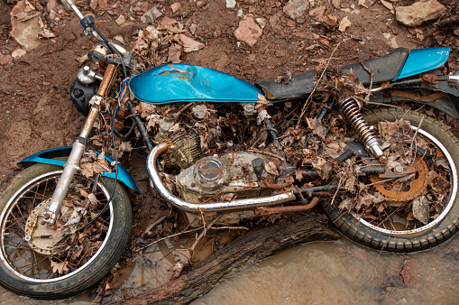 Abandoned blue motorcycle in the mud and creek