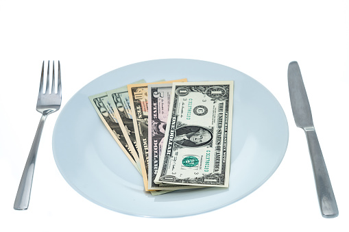 USA dollar currency banknotes on a dinner plate representing the increasing cost of dining  out - white background