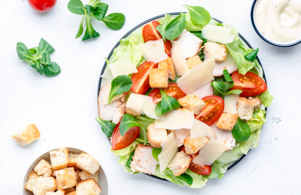Caesar salad with chicken, iceberg salad, croutons, parmesan cheese and tomatoes with caesar dressing. White table background, top view stock photo