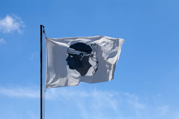 Corsican flag waving atop of its pole against a blue sky.