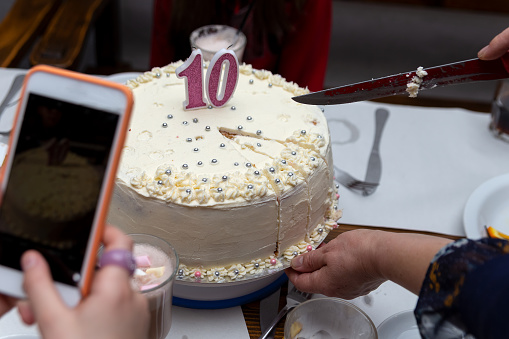 There is a birthday cake on the table. Which the woman cuts with a knife.