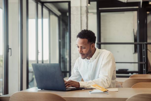 Young man working in an office 4k video footage of a young man using his laptop while working in his office black man laptop stock pictures, royalty-free photos & images