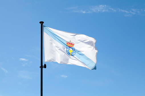 Flag of Galicia waving atop of its pole against a blue sky.