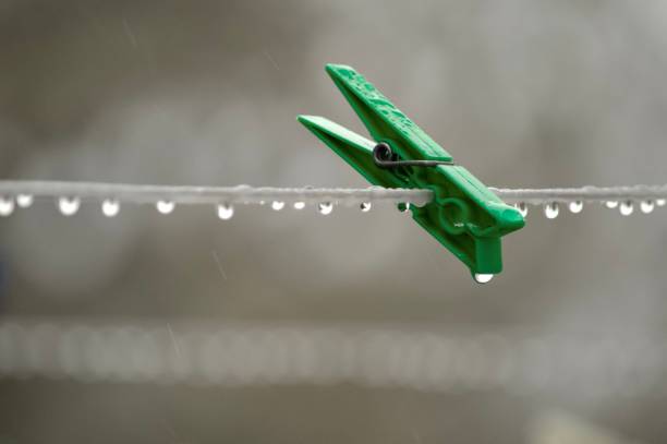 Green clothespin hanging on the clothesline in the rain, stick, hope, loneliness, hanging by a thread minimal concept