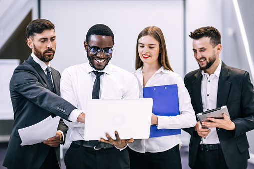 African American businessman Boss with a group of business people in a creative office, a successful man and managers are holding documents and looking into a laptop.