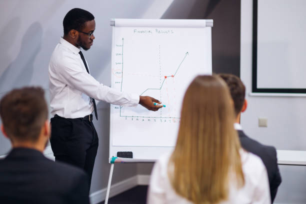 istock Serious African American mentor giving presentation explains sales growth graph by teaching different trainees in group meeting, new corporate plan on flipchart 1473530159
