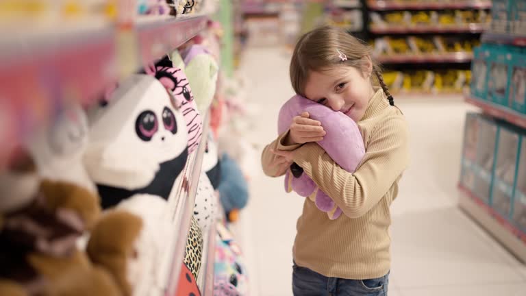 The girl is standing in a children's toy store in front the shelf and take a soft toy