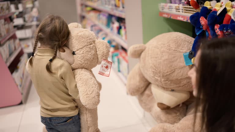 Mother gives big soft bear toy to her daughter in children's department store