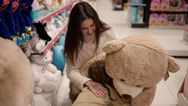 Mother shows big soft bear toy to her daughter in children's department store