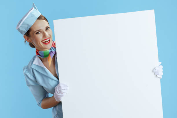 aeromoça feminina moderna sorridente no azul mostrando a placa em branco - mature women outdoors smiling happiness - fotografias e filmes do acervo