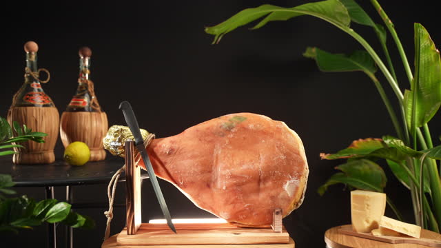 Fat jamon on wooden stand with knife, traditional cured ham served with parmigiano cheese, Italian or Spanish prosciutto leg ready for slicing