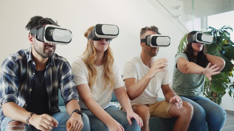 Four friends are using virtual reality glasses together on the sofa at home