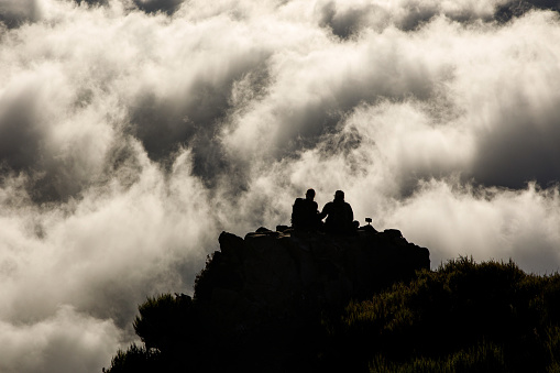 Two people on top of a mountain above the clouds.