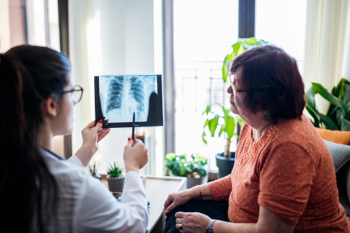Young female doctor on a home visitation showing a senior patient an X-ray image of her lungs.