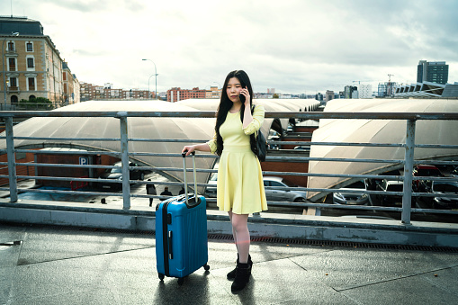 a girl with her blue suitcase talking on the phone dressed in yellow
