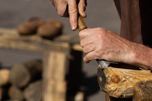Detail of the hands of an artisan carpenter carving with blurred background.