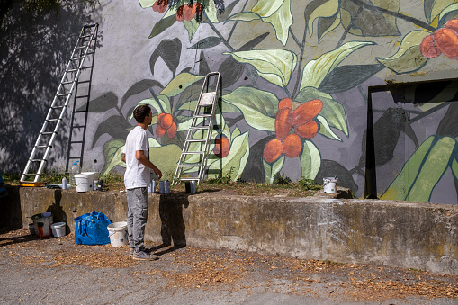 A graffiti artist paints graffiti on a large retaining wall.