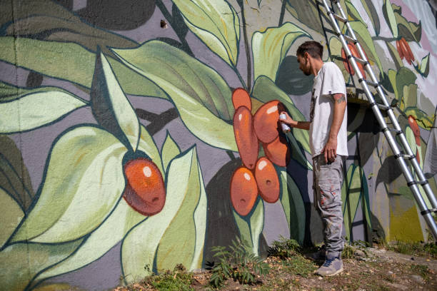 ein graffiti-künstler malt graffiti auf eine große stützmauer. - straßenmaler stock-fotos und bilder