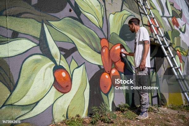 A Graffiti Artist Paints Graffiti On A Large Retaining Wall Stock Photo - Download Image Now