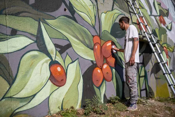 A graffiti artist paints graffiti on a large retaining wall.