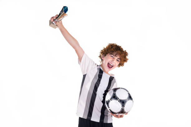 istock Excited boy with soccer ball and trophy in a white background in a studio 1473543228