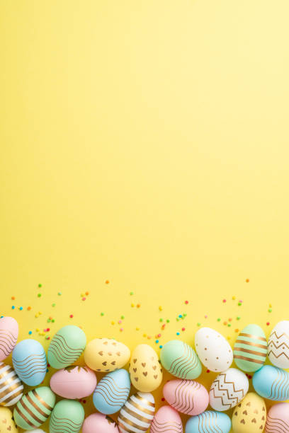 istock Easter celebration concept. Top view vertical photo of colorful easter eggs and confetti on isolated yellow background with copyspace 1473544429