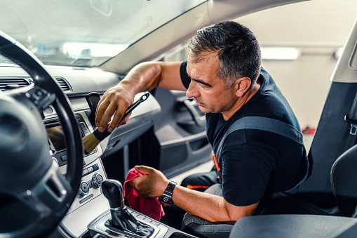 Professional worker cleaning car interior and dashboard