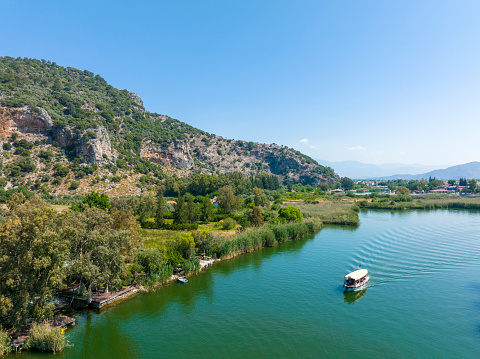 Dalyan - Mugla - Turkey, October 22, 2021, Rock-cut temple tombs of the ancient city Kaunos in Dalyan, Mugla, Turkey. Beautiful Dalyan river view with ferry boats and carved tombs at background.