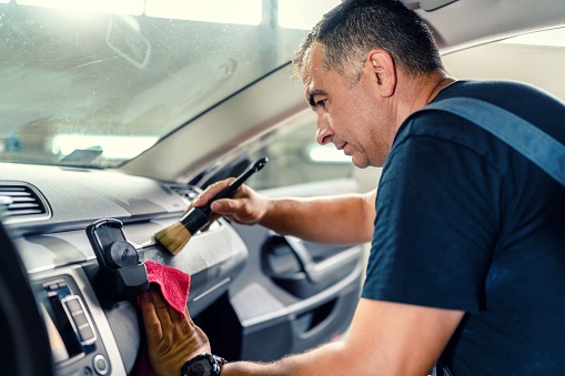 Professional worker cleaning car interior and dashboard
