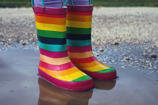 Feet of child in colorful rubber boots standing over puddle.