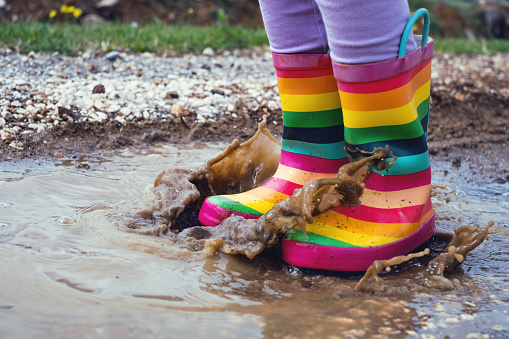 Feet of child in colorful rubber boots jumping over puddle.