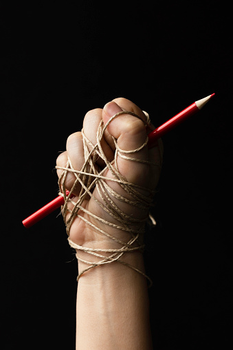 Hand holding red pencil and is tied up with rope. Representing freedom speech, freedom of expression issues.