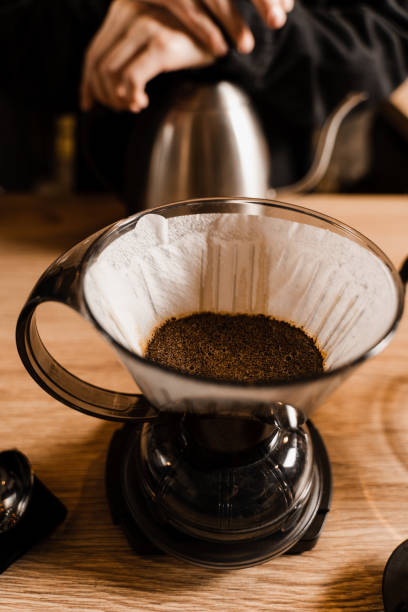 istock Clever coffee dripper with pour over filter with ground coffee in the funnel in focus. Drip filter coffee brewing. Pour over alternative method of pouring water over coffee beans contained in filter. 1473554167