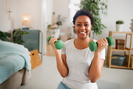 Portrait of young beautiful woman holding dumbbels and posing for a shot during workout at home