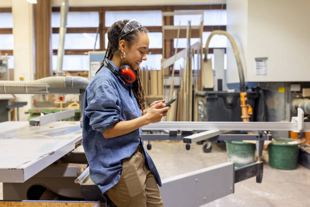 istock Woman worker textping on cell phone during a break at a carpentry worksho 1473557854