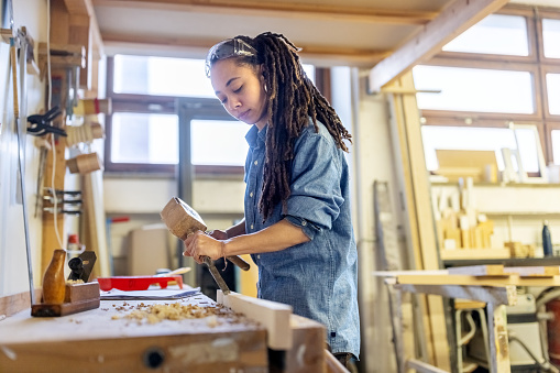 Carpenter woman carving wood with tools in workshop. Woman carpenter working with a mallet and chisel carving wood.