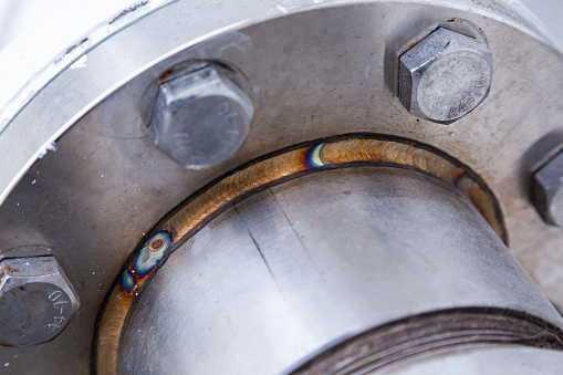 A section of a welded pipe with a stainless steel flange with screwed-in bolts.