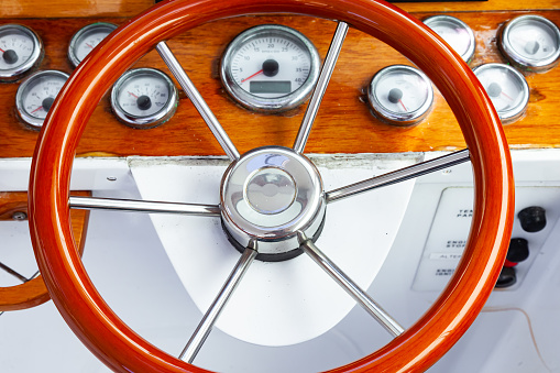 The cockpit of a luxury yacht with a classic, circular steering wheel and navigation equipment.