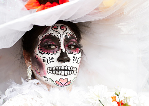 Oceanside, CA—10/30/2016: A woman in an elaborate dress and hat has her face painted as a skull for the Day of the Dead. The Day of the Dead is a traditional day of remembrance in the Mexican culture for those who have passed away. During this day, people visit the graves of relatives and leave gifts and flowers.