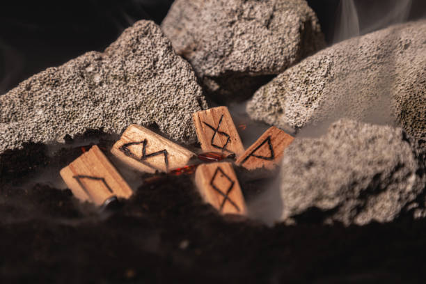 the wooden rune of Inguz among other runes, symbols of the earth, lie in the ground amid smoke and large stones. Mysticism and the rite of fruitful earth the wooden rune of Inguz among other runes, symbols of the earth, lie in the ground amid smoke and large stones. Mysticism and the rite of fruitful earth symbolism stock pictures, royalty-free photos & images