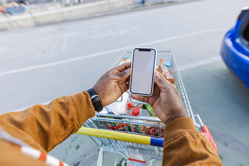 African-American man holding a smart phone and pulling a shopping cart