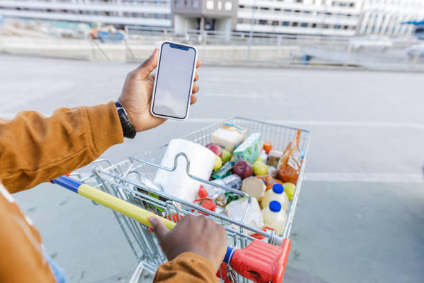 istock Personal perspective of a man holding smart phone with a white screen and pulling a shopping cart 1473567671