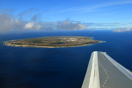 Nauru island: the entire country seen from above - Island surrounded by the coral reef - the oval island has a narrow coastal belt where settlements are located, the interior known as 'topside' is  a barren plateau of jagged limestone pinnacles due to the environmental damage caused by phosphate mining - South coast and Meneng district in the foreground, Aiwo, Yaren and the airport on the left, Anibare Bay on the right - South Pacific Ocean.