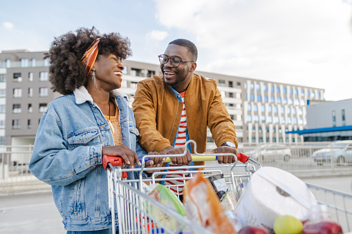 Smiling young African-American couple on a Supermarket parking with shopping cart