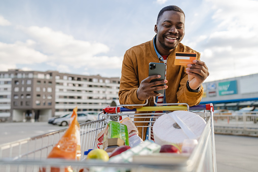 A smiling young African-American man walking and using online paying services