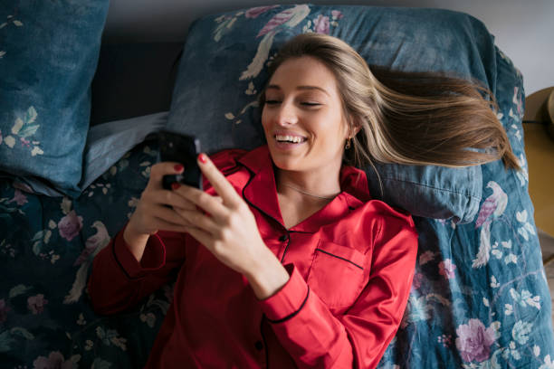 istock Smiling woman relaxing on bed at home and using smart phone 1473574807