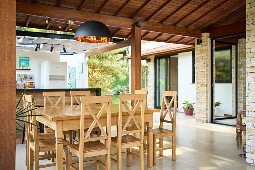 Dining table and chairs sitting by an outdoor kitchen on the patio of of a modern home in the summer